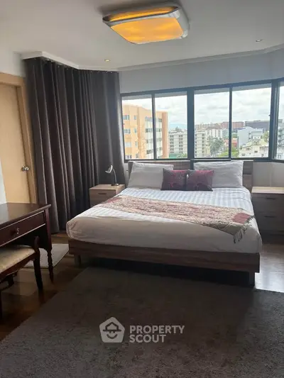 Spacious bedroom with large windows offering stunning city views and elegant decor.