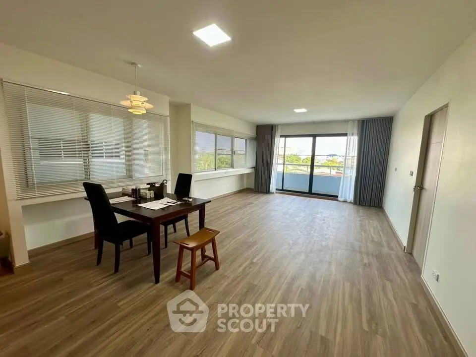 Spacious open-plan living room with large windows and balcony access, featuring modern flooring and elegant dining setup.