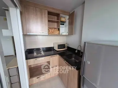 Modern compact kitchen with wooden cabinets and black countertops, featuring a microwave and stainless steel fridge.