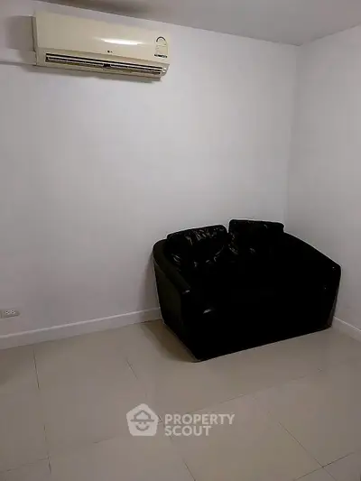 Minimalist room with black leather sofa and wall-mounted air conditioner.