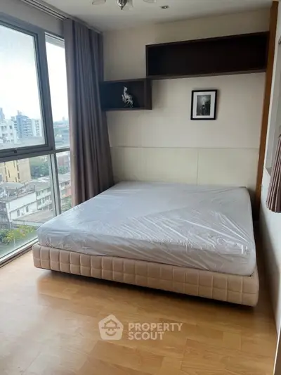 Cozy bedroom with large window offering city views, featuring a comfortable bed and stylish decor.