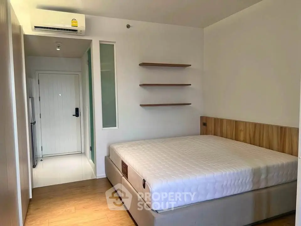 Modern minimalist bedroom with wooden flooring and built-in shelves, featuring a comfortable bed and air conditioning.