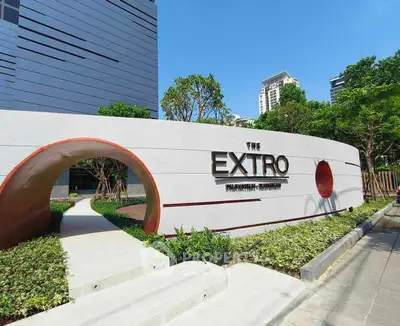 Modern building entrance with stylish signage and lush landscaping in urban setting.