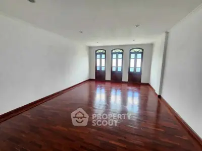 Spacious empty room with elegant wooden flooring and classic French doors.