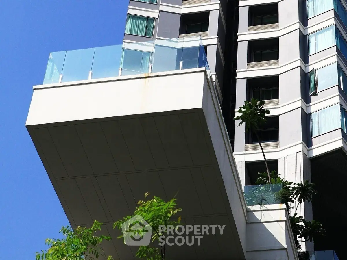 Modern high-rise building with spacious balcony and glass railings against clear blue sky.