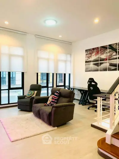 Spacious living room with modern decor and natural light, featuring cozy seating and a stylish workspace.