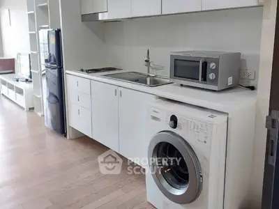Modern kitchen with washing machine, microwave, and sleek cabinetry in a bright apartment.