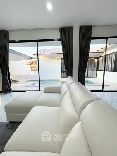 Modern living room with white sofa and pool view through large windows.