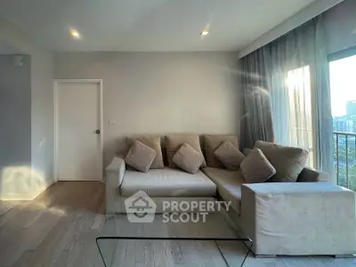 Spacious living room with modern beige sofa and glass coffee table, featuring large windows with city view.