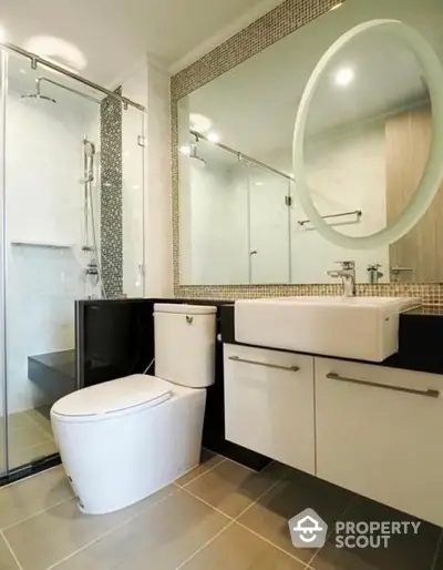 Modern bathroom with sleek design, featuring a frameless glass shower, stylish round mirror, and contemporary vanity with ample storage.