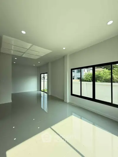 Spacious modern living room with large windows and glossy tiled floors, offering abundant natural light.