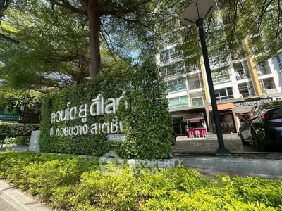 Modern condominium entrance with lush greenery and sleek building facade.