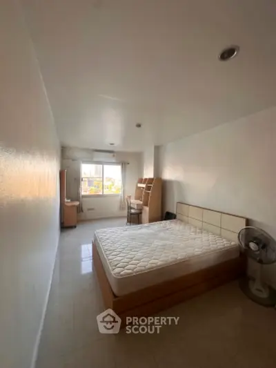 Spacious bedroom with natural light and city view, featuring modern furniture and minimalist design.