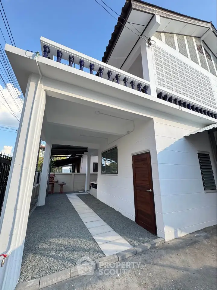 Modern two-story house with white exterior and wooden door, featuring a covered driveway and contemporary design.