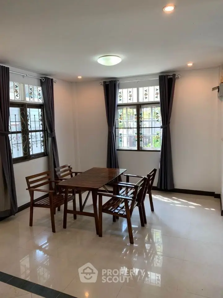 Bright dining area with wooden table and chairs, large windows and elegant curtains.