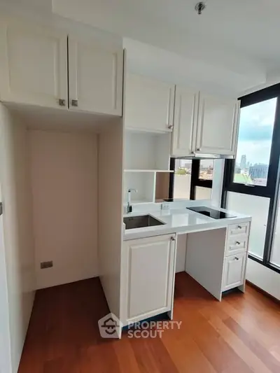 Compact kitchen with white cabinets and large window offering city view