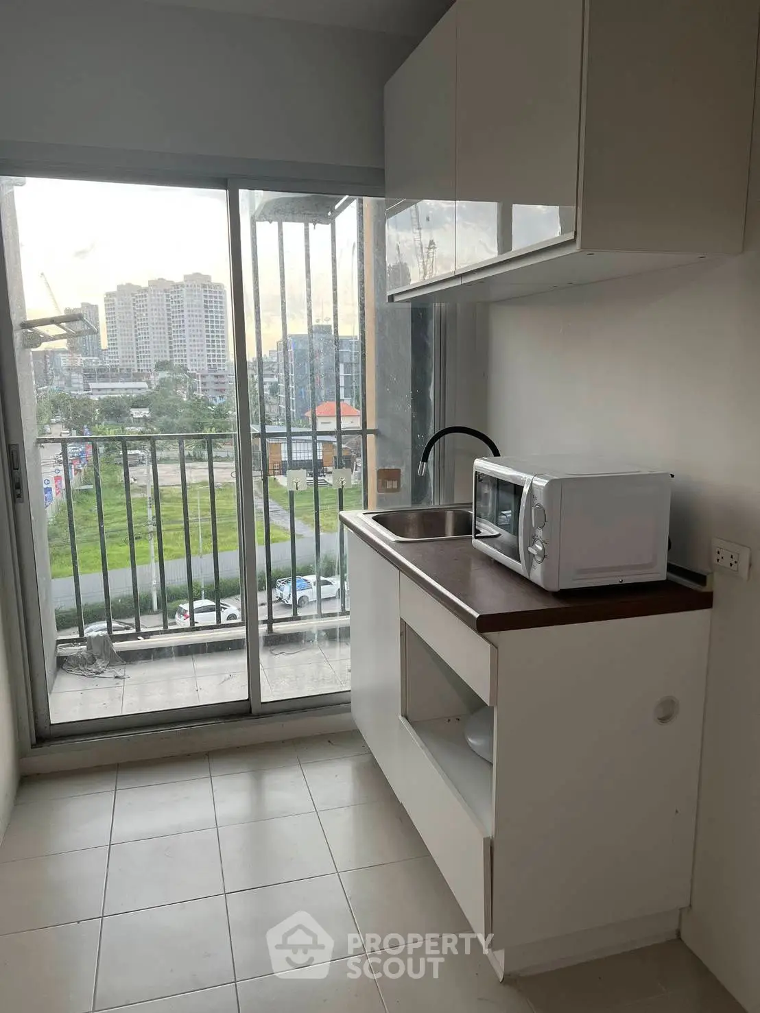 Compact kitchen with balcony view, featuring modern appliances and sleek cabinetry in urban apartment.