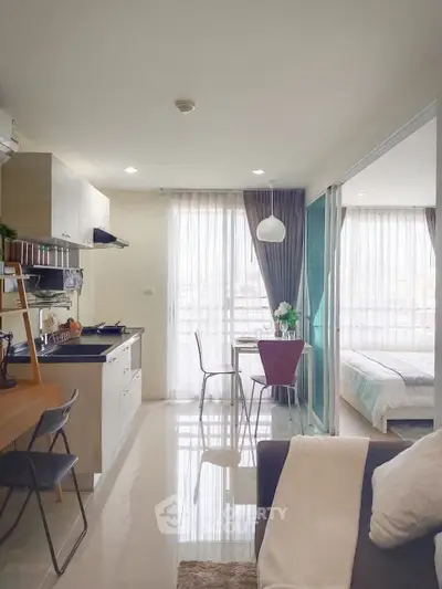 Modern open-plan apartment with kitchen, dining area, and bedroom featuring large windows and natural light.
