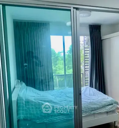 Cozy bedroom with large window and sliding glass doors, offering a serene view of greenery.