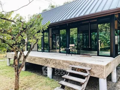 Modern elevated house with glass walls and lush garden surroundings