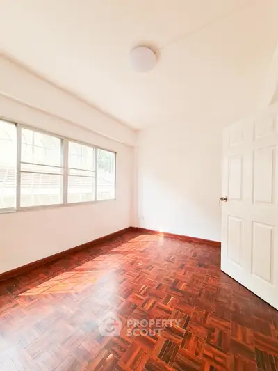 Bright empty room with wooden flooring and large windows, perfect for customization.