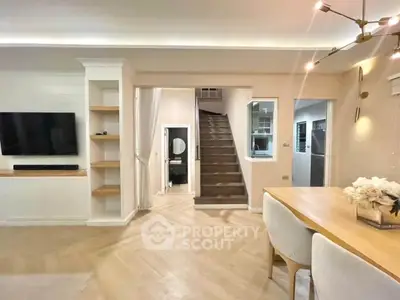 Modern living room with elegant dining area and staircase, featuring stylish lighting and built-in shelving.