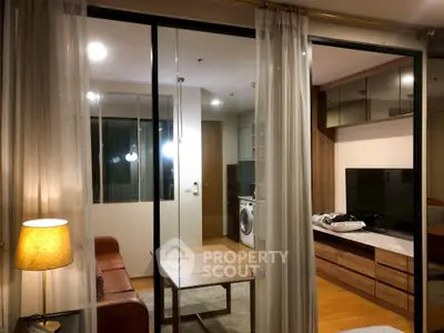 Modern living room with glass partition, cozy seating, and washing machine in view.