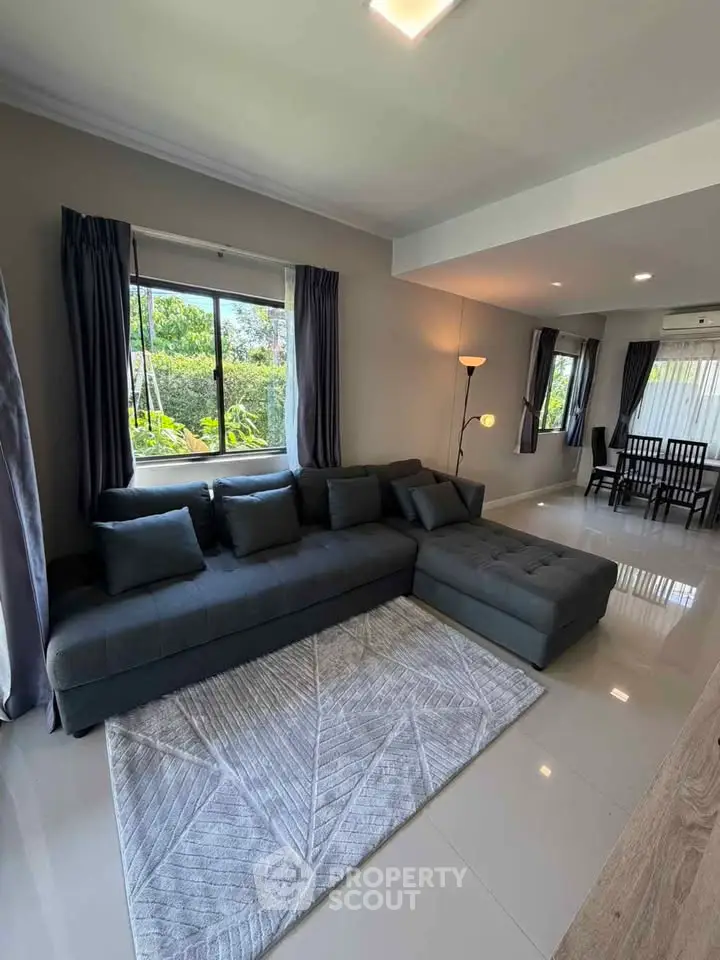 Spacious living room with modern sectional sofa and large windows overlooking greenery.