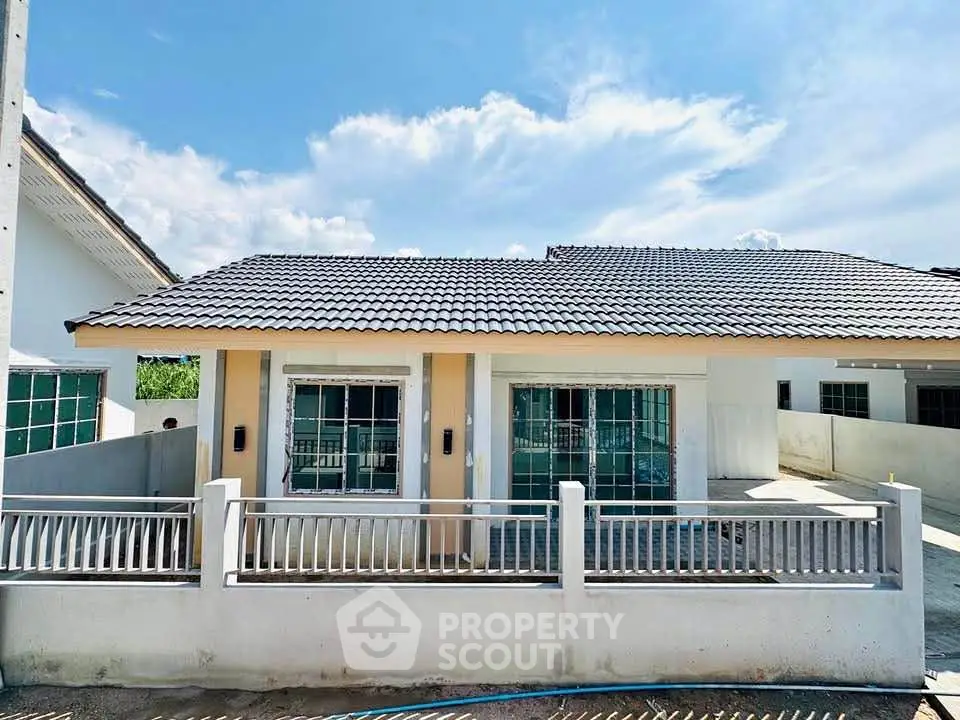 Charming single-story house with tiled roof and fenced yard under a bright blue sky.