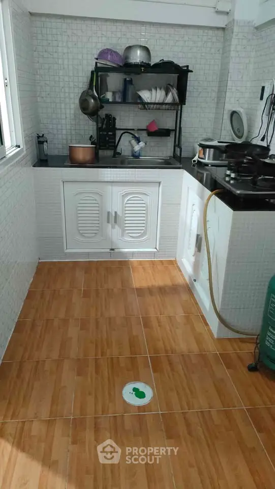 Compact kitchen with tiled walls and wooden flooring, featuring a gas stove and storage cabinets.