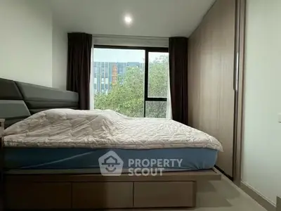 Modern bedroom with large window and built-in wardrobe, offering a serene view of greenery.