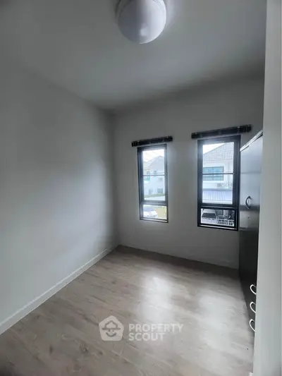 Compact bedroom with large windows and wooden flooring, ideal for cozy living.