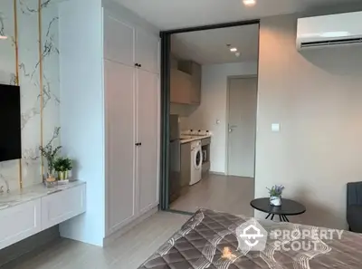 Modern studio apartment with sleek design, featuring an integrated living space with a cozy bed area, a compact kitchen with modern appliances, and a neatly tucked away laundry unit.