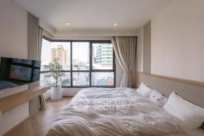 Modern bedroom with large windows and city view, featuring cozy bedding and stylish decor.