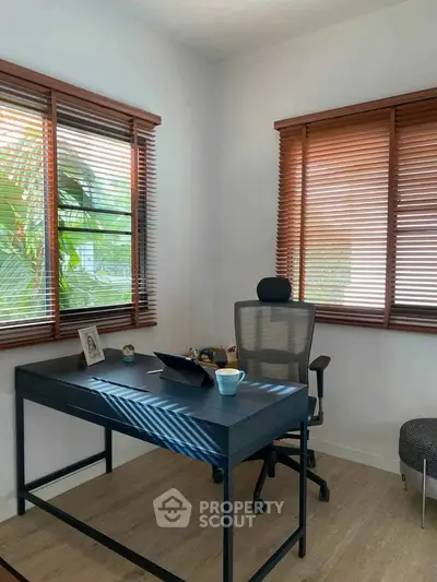 Bright home office with modern desk and ergonomic chair, featuring large windows with wooden blinds.