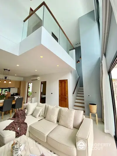 Modern open-plan living room with high ceilings and mezzanine, featuring a cozy beige sofa and stylish decor.