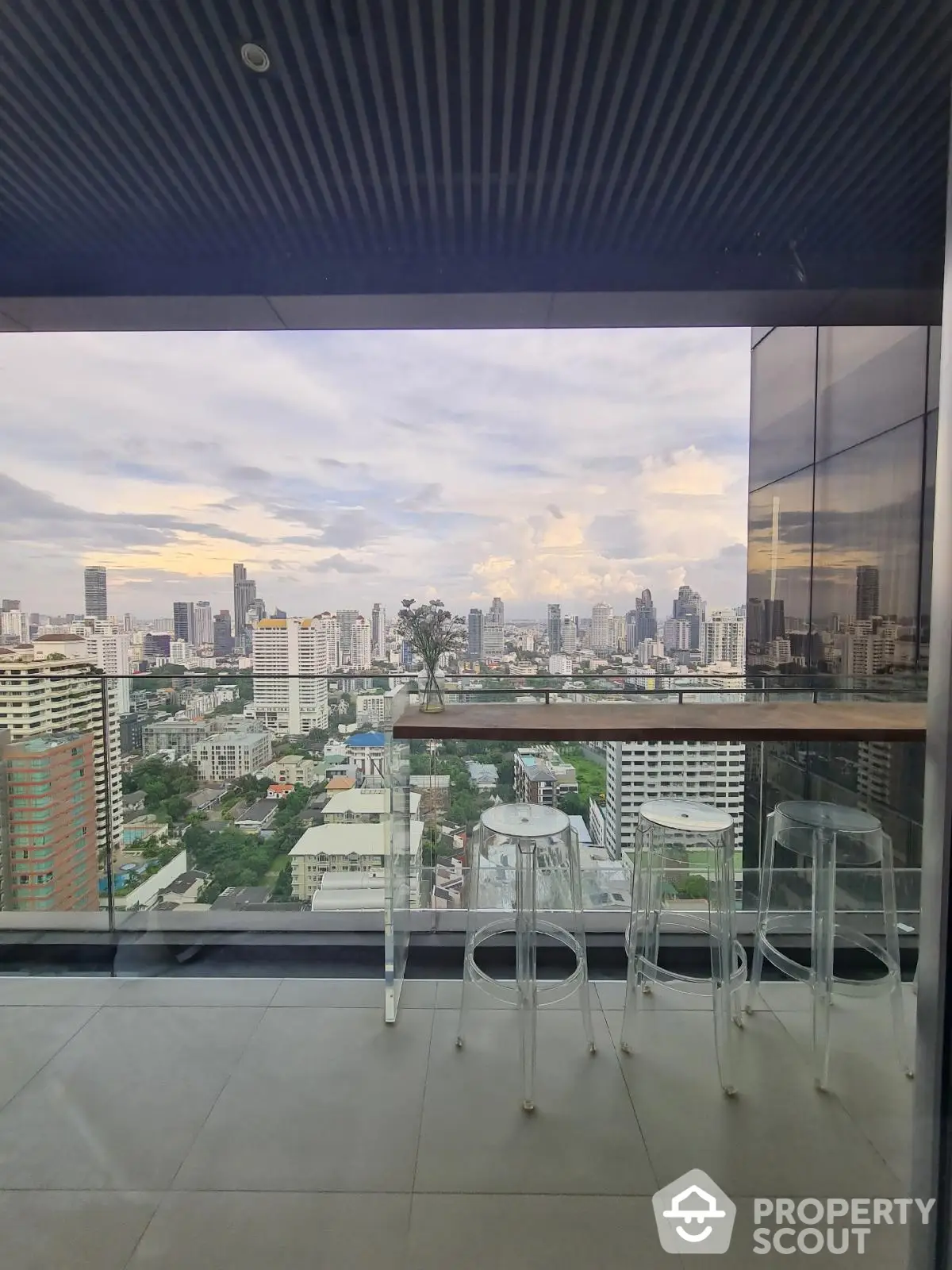 Stunning cityscape view from modern high-rise balcony with sleek glass railing and stylish seating.