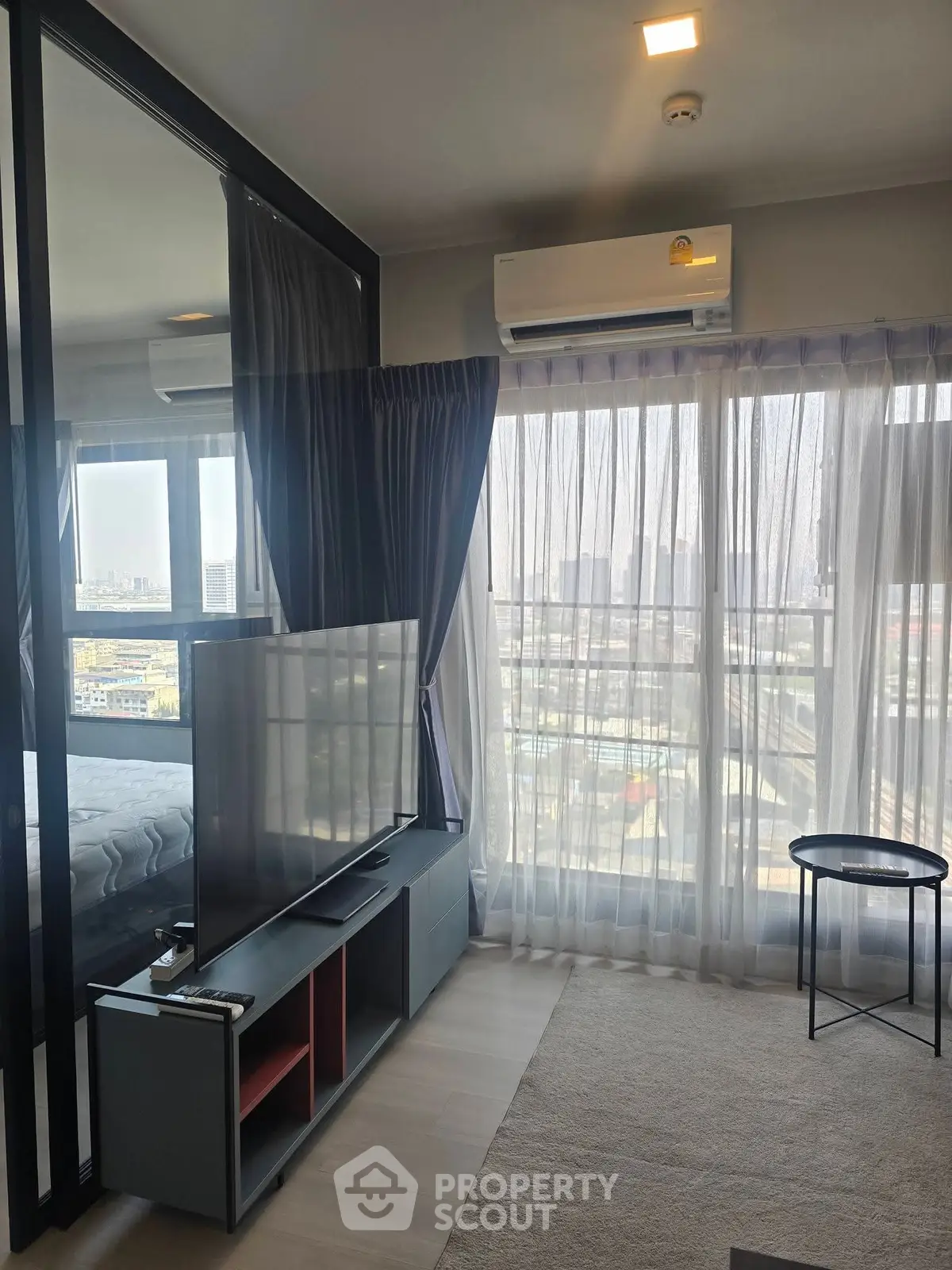 Modern living room with large TV and city view through glass doors