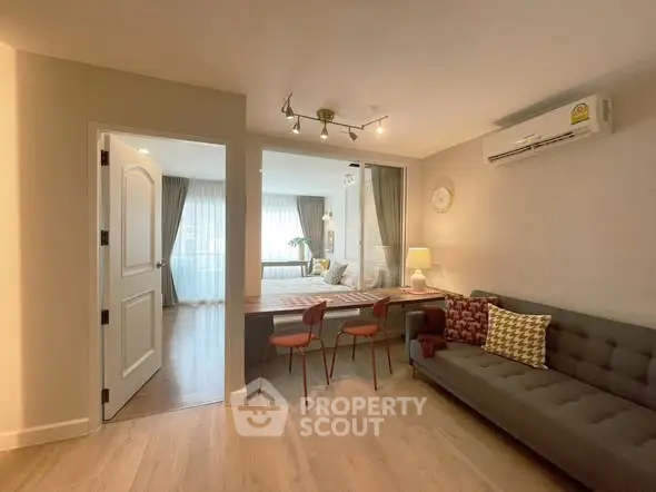 Modern living room with stylish decor and cozy seating area, featuring a view into a bright bedroom.