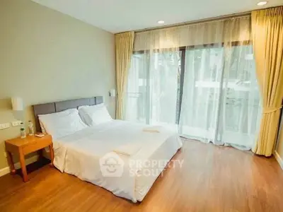 Spacious bedroom with large windows and elegant curtains in modern apartment.