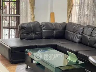 Spacious living room with elegant black leather sofa and glass coffee table, perfect for relaxation.