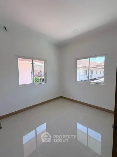Bright empty room with tiled floor and two windows showcasing neighborhood view.