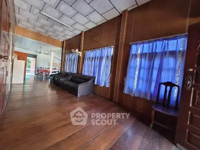 Spacious living room with wooden floors and blue curtains, featuring a cozy black sofa.