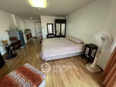 Spacious studio apartment with modern furnishings and wooden flooring, featuring a cozy bed and compact kitchen area.