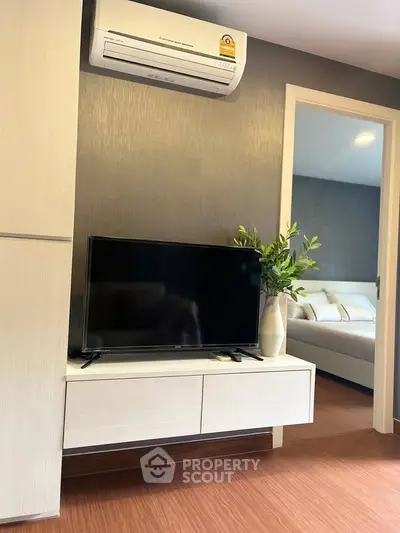 Modern living room with sleek TV setup and air conditioning, leading to a cozy bedroom.
