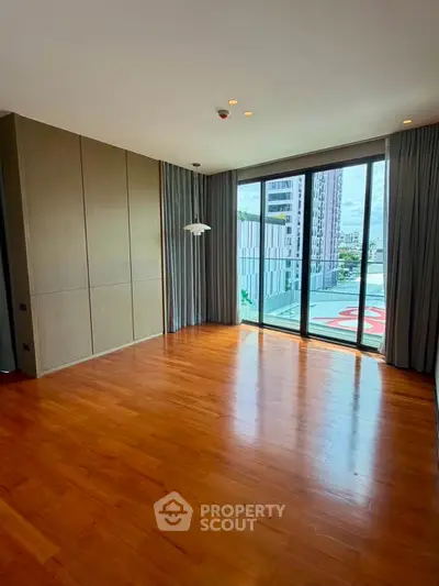 Spacious living room with wooden flooring and large windows offering city views.