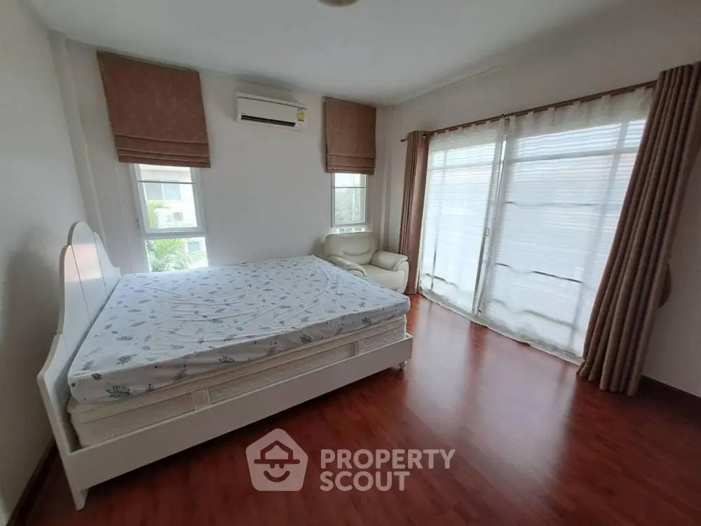 Spacious bedroom with large windows and elegant curtains, featuring a comfortable bed and wooden flooring.