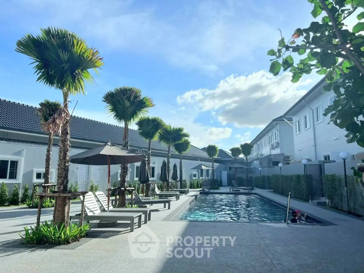 Luxurious residential complex with a pristine swimming pool and lush palm trees under a clear blue sky.