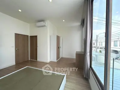 Spacious modern bedroom with large window and wooden flooring in a contemporary home.