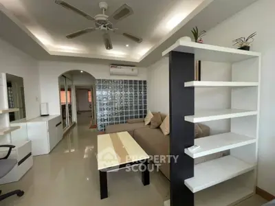 Modern living room with sleek furniture and ceiling fan, featuring glass block wall for stylish ambiance.